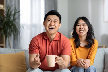 Mutlu Asyalı orta yaşlı koca ve genç güzel eş oturma odasında kanepede oturur, sarılırlar, film izlerler, çay içerler, neşeli Koreli kadın ve erkek TV şovundan zevk alırlar, uzay kopyalarlar.