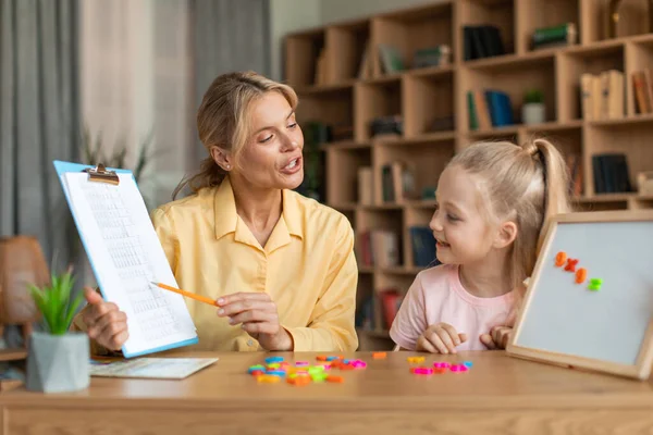 Professional female teacher exercising with clever preschool girl, little child counting and repeating words and numbers. Child development school concept