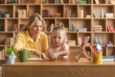 Sevimli küçük kız mektup öğreniyor ve profesyonel öğretmenle okumak için okuyor, pozitif öğretmen çocuğa yardım ediyor, anaokulunda birlikte okuyorlar.