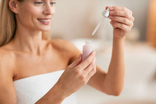 Beauty and skincare concept. Middle aged woman holding and opening bottle with moisturizing face serum, making skin treatment at home, cropped, copy space