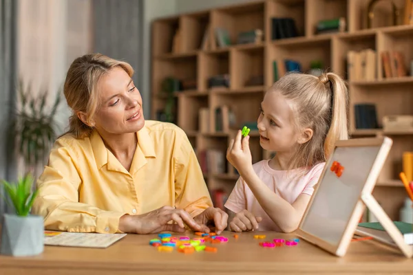 Foreign language classes for preschoolers. Clever pretty kid girl learning alphabet, pronouncing and making words with colorful English letters on board