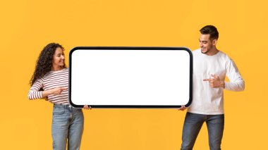 Mobil Teklif. Orta Doğu 'lu erkek ve kadın ellerinde beyaz ekranlı cep telefonu tutuyorlar, sarı arka planda duruyorlar, Mockup' ı çekiyorlar.