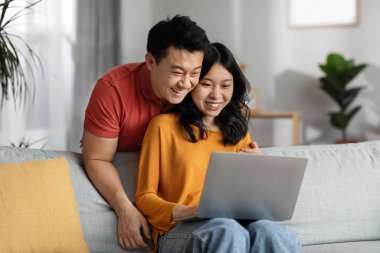 Asyalı orta yaşlı bir adam ve genç bir kadın defter ekranına bakıyor. Güzel Çinli bir kadın, neşeli kocasının fotoğraflarını internette ya da internette gösteriyor.