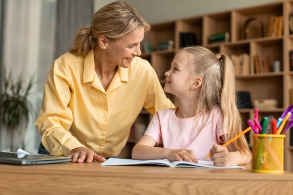 어머니와 귀여운 책상에 웃으면서 사랑많은 어머니는 자녀가 숙제를 하도록 — 스톡 사진