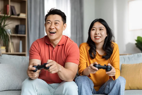 快乐的韩国夫妇在家里玩电子游戏 快乐的中年男子和漂亮的年轻女子坐在沙发上 手握操纵杆 复制空间 家庭娱乐概念 — 图库照片
