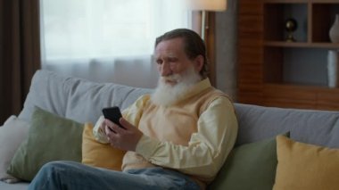 İnternet ve yaşlılar. Sakin sakallı yaşlı adam internette sörf yapıyor, evdeki kanepede dinleniyor, dünya haberleri okuyor, yavaş çekim, serbest alan