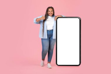 Şişman, neşeli, şişman bir kadın, parmaklarını havaya kaldırıyor, Pembe Arkaplan Üzerine Mobil Teklif Veren Akıllı Telefon Boş Ekran 'a yaslanıyor. Stüdyo Çekimi