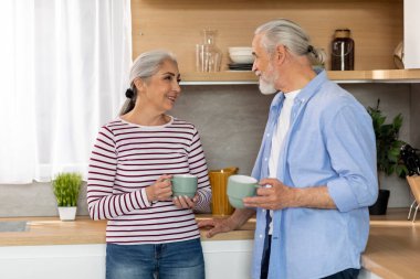 Ev Tatili. Gülümseyen kıdemli eşlerin portresi mutfak içinde kahve içerken mutlu yaşlı çiftin evde birlikte dinlenmesi sıcak içkinin tadını çıkarması ve birbirleriyle sohbet etmeleri, boş bir alan.