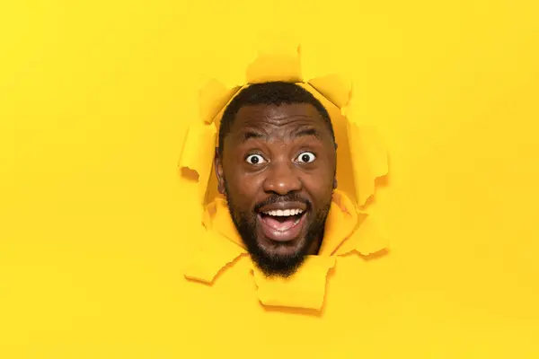 Радостный Черный Человек Стоящий Через Разорванную Дыру Желтого Фона Удивленно — стоковое фото