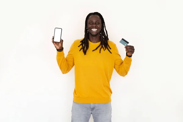 网上银行 快乐黑人男子持信用卡和空白智能手机站在白色背景下 笑着向美国黑人男性推荐电子商务应用 — 图库照片