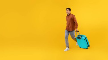 Mavi bavullu mutlu turist sarı stüdyo arka planında mesajlaşmak için boş alana bakıyor. Erkek Reklamcılık Seyahat Teklifi. Panorama, Tam Uzunluk Görüntüsü