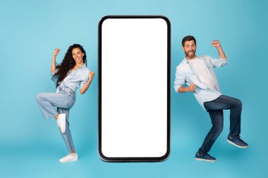 Mutlu uluslararası erkek ve kadın dansları, mavi arka planda, stüdyoda izole edilmiş, boş ekranlı akıllı telefonun yanında kazanmaktan mutluluk duyarlar. Zafer online, yeni uygulama, aygıt, teklif, reklam ve satış