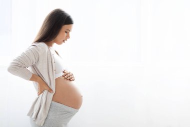 Hamilelik, ebeveynlik kavramı. Beyaz arka planda poz veren, ev elbiseli, hamile bir kadının koca göbeğine dokunduğu, fotokopi alanı olan bir panorama.