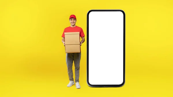 Aplicação Entrega Courier Guy Posando Perto Enorme Celular Tela Branco — Fotografia de Stock