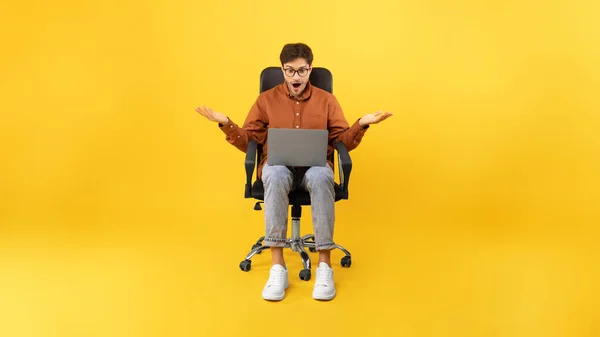 Wow Offer. Shocked Man Using Laptop Working Online Sitting In Office Chair Posing On Yellow Studio Background. Internet Technology And Business Concept. Panorama