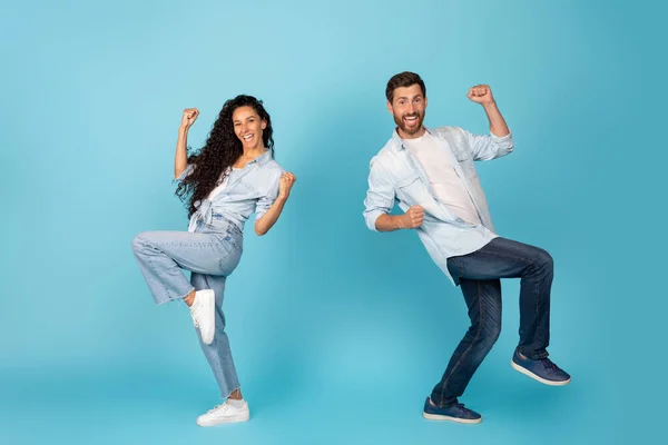 Satisfied excited young caucasian and arab people rejoice to success, dance and make victory gesture, isolated on blue background, studio, promo. Human emotions, win, mockup, great offer ad and sale