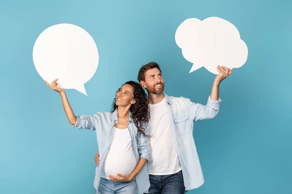 Happy young european man and arabic pregnant woman holding abstract clouds, bubbles with empty space, isolated on blue background, studio. Great offer, ad and sale, good idea and thinks for future kid