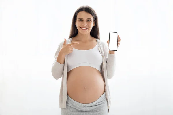 幸せな美しい妊娠中の女性とともに大きなおなかのホームウェアショー携帯電話で白い空の画面 お勧めします素敵なモバイルアプリ 白い背景 広告のためのモックアップ コピースペース — ストック写真