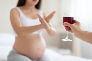 Hamilelik sırasında alkol yasak. Tanımlanamayan hamile kadın şarap içmeyi reddediyor, bardağa kırmızı içecekle jest yapıyor, evde oturuyor, boş yer, kırpılmış mermi.
