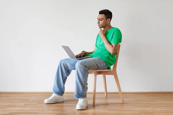 Troubled arab man sitting on chair with laptop, making mistake in online project, thinking over solution to problem against white wall, copy space. Banner design