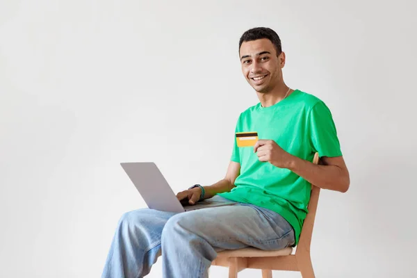 快乐的男性买家使用笔记本电脑和信用卡 在网上付款 坐在白墙上方的椅子上 自由自在 使用网上银行的客户 电子商务概念 — 图库照片