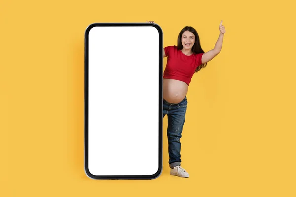 Mooie Promotie Positieve Zwangere Vrouw Gluren Achter Big Blank Smartphone — Stockfoto