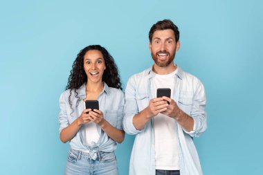 Bin yıllık beyaz sakallı ve Arap kadınlı bir adam akıllı telefonlarla sohbet ediyor, mavi arka planda, stüdyoda izole edilmiş. Harika reklam ve teklif, yeni blog ve uygulama, online kazanç ve haberler