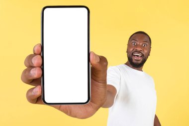 Vay canına. Heyecanlı Siyah Adam Cep Telefonunu Boş Ekran Ekranı ile Gösteriyor Yeni Uygulamayı Öneriyor Sarı Arkaplan Üzerinde Kamera Pozisyonuna Kolunu Geriyor. Stüdyo Çekimi, Model