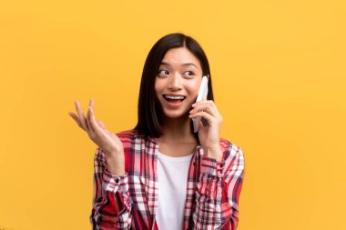 Neşeli, pozitif Asyalı kadın, sıradan hareketler yapıyor ve akıllı telefondan arıyor, sarı arka planda izole edilmiş, stüdyo çekimi. Harika reklam ve teklif, dedikodu, iyi haber ve satış.