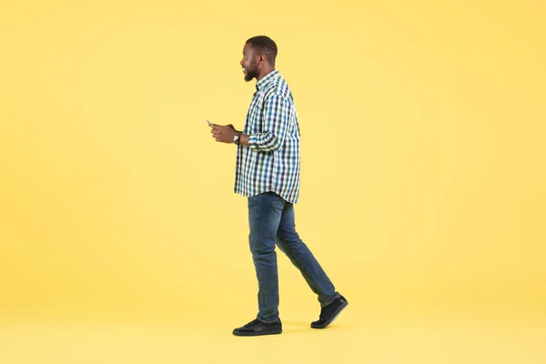 非裔美国人通过电话申请 发短信在黄色背景下行走 演播室拍摄 移动提供广告概念 侧视图 — 图库照片
