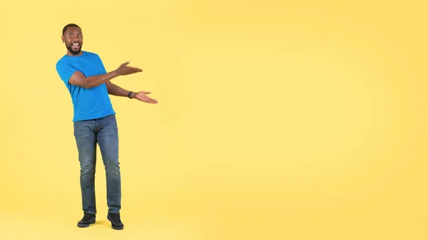 看那里 兴奋的黑人男子与双手展示空白空间文字广告提供站在黄色工作室背景的相机微笑 — 图库照片