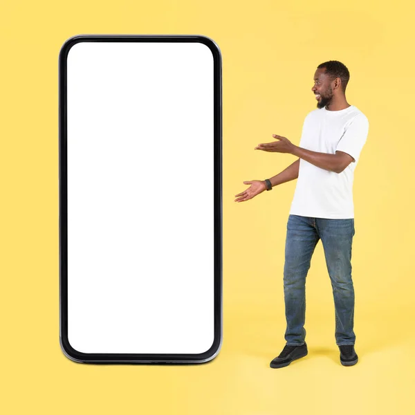 美国黑人男子展示大手机与空屏幕站在工作室黄色背景 伟大的移动提供 新的应用广告 正方形射击 莫科普 — 图库照片