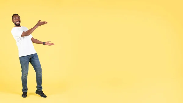 快乐的黑人男性展示自由空间为文字广告大报价站在镜头前 在黄色的工作室背景下拍照 全长镜头 — 图库照片
