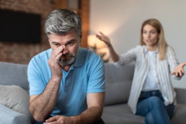 Kızgın orta yaşlı Avrupalı kadın oturma odasının içinde kavga ederken gücenmiş bir adamı azarlıyor, kapat. Skandal, stres ve duygular, ilişki sorunları ve evde covid-19 salgını nedeniyle taciz