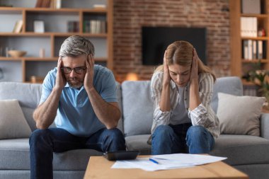 Yoksul orta yaşlı Avrupalı çift oturma odasının içindeki faturalardan muzdarip. Küresel kriz, stres ve evrak işleri, iflas, mortgage ve vergi ödeme, muhasebe, ilişki sorunları