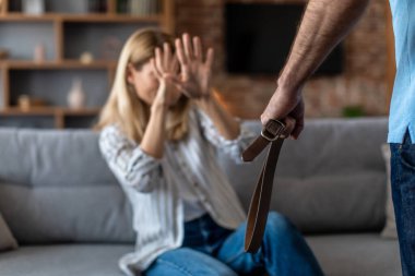 Orta yaşlı avrupalı kadın oturma odasında kemeri olan saldırgan bir adamdan dayak yiyor. Aile içi şiddet, ilişki sorunları, covid-19 sırasında evde stres ve duygular