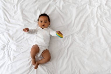 Evde yatakta çıngıraklı yılanla oynayan sevimli siyah bebek, yatak odasında beyaz çarşafların üzerinde dinlenen siyah çocuk portresi.