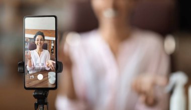 Ünlü güzellik blogcusu evden yayın yapıyor, akıllı telefon ekran kayıt videosuna odaklanıyor, güzellik ürünleri öneren güzel bir genç kadın, bulanık bir arka plan, panorama