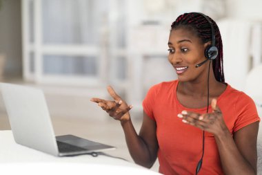 Telekonferans Konsepti. İç İşleri 'nde çalışırken bilgisayarında video görüşmesi yapan kulaklıklı genç siyahi kadın, web kamerasına gülümseyen ve hareket eden Afrikalı Amerikalı kadın,