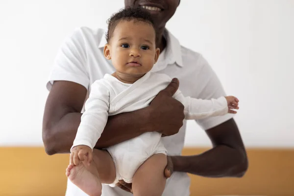 Young Black Father Holding Cute Little Baby Boy In Hands, Loving African American Dad Embracing His Small Infant Son And Smiling, Bonding With Adorable Newborn Child At Home, Closeup Shot