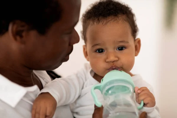 Adorable Little Black Baby Drinking Water Bottle While Relaxing Fathers — Stock Photo, Image