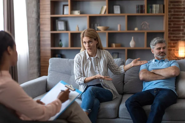 不幸な中年ヨーロッパの女性は心理学者室内のソファの上で男性を怒らせることを示しています 関係の問題 家族の危機 医療支援と専門家の助けとの出会い — ストック写真