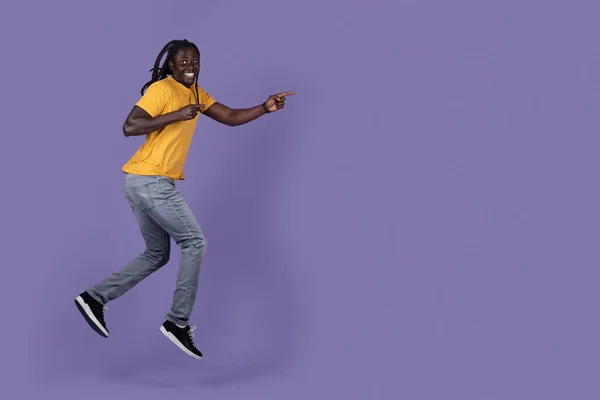 黄色のTシャツを着た長いブライドを持つ陽気なアフリカ系アメリカ人の若者が走っていて 紫色のスタジオの背景 パノラマ上の広告のためのコピースペースを指しています オファー ニュース — ストック写真