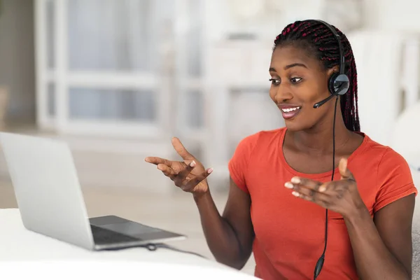 テレビ会議の概念 自宅で働いている間にノートパソコンでビデオ通話をするヘッドフォンの若い黒人女性 Webカメラで話しているアフリカ系アメリカ人女性を笑顔とジェスチャー スペースをコピー — ストック写真