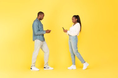 Siyah adam ve kadın akıllı telefonlar kullanarak interneti tarıyor ve sarı stüdyonun arka planında duruyor, uzun çekim. Yeni Mobil Uygulama Reklamı