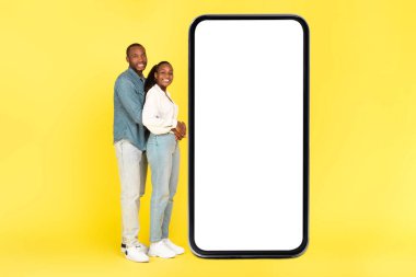 Sarı Stüdyo Arkaplanında Beyaz Ekran Reklam Teklifi ya da Mobil Uygulamalı Büyük Akıllı Telefona Kucaklaşan Afro-Amerikan Çifti. Mockup, Tam Uzunluk Çekimi