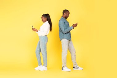 Stüdyoda arka arkaya mesajlaşan ve internetteki sarı arkaplan pozlarını tarayan akıllı telefonları kullanan Afrikalı Amerikalı çift. Mobil Teklif, Uygulama Reklam Konsepti. Tam Uzunluk