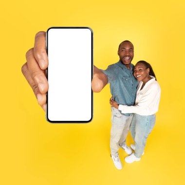 Neşeli Siyah Eşler, Sarı Stüdyo Arkaplanındaki Mobil Mobil Reklam Arkaplanına Boş Ekranla Büyük Akıllı Telefonları Gösteriyor. Vay canına başvuru formu. Mockup, Kare Vuruş