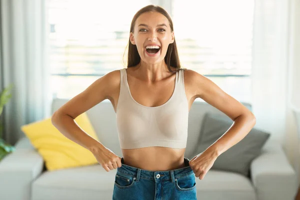 Slim Female Laughing Celebrating Successful Weight Loss Showing Great Result Wearing Old Large Jeans For Comparison Smiling To Camera Standing At Home. Slimming And Dieting