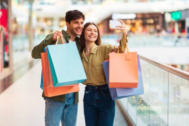 Satış teklifi. Mutlu müşteriler alışveriş yapıyor ve cep telefonuyla selfie çekiyor. Modern alışveriş merkezlerinde eğleniyorlar. Alıcılar telefonda alışveriş torbalarıyla fotoğraf çektiriyorlar. Alışveriş Konsepti